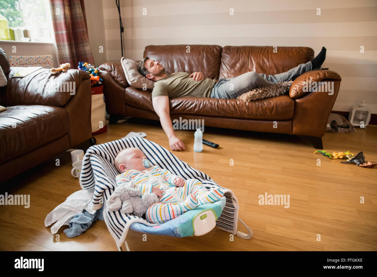 Épuisé père ayant une sieste sur le canapé tandis que son enfant nouveau-né a un sommeil. Banque D'Images