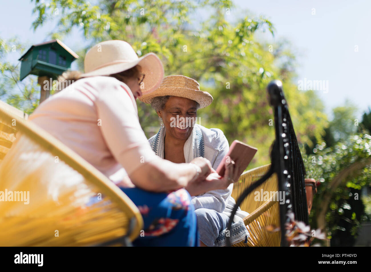 Les femmes âgées des amis à l'aide de smart phone sur patio ensoleillé Banque D'Images