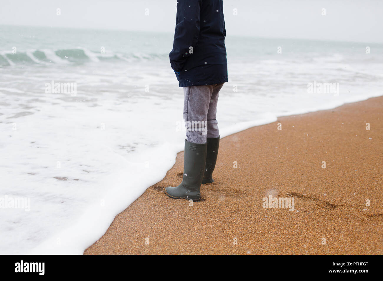 En bottes de caoutchouc garçon debout à Océan surf sur la plage d'hiver  Photo Stock - Alamy