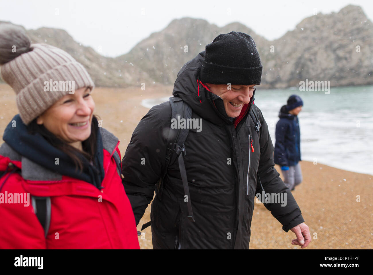 Smiling couple dans des vêtements chauds d'hiver enneigés sur beach Banque D'Images