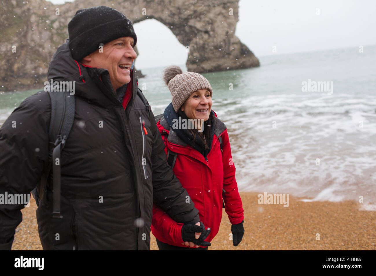 Couple heureux dans des vêtements chauds marche sur la plage de l'océan de neige Banque D'Images