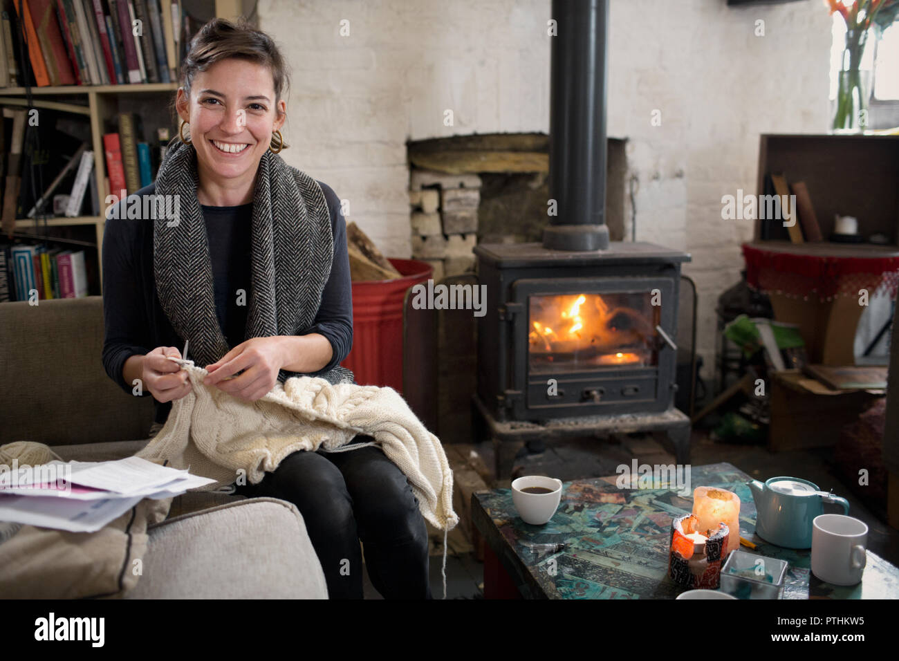 Portrait souriant, woman knitting par foyer au salon Banque D'Images