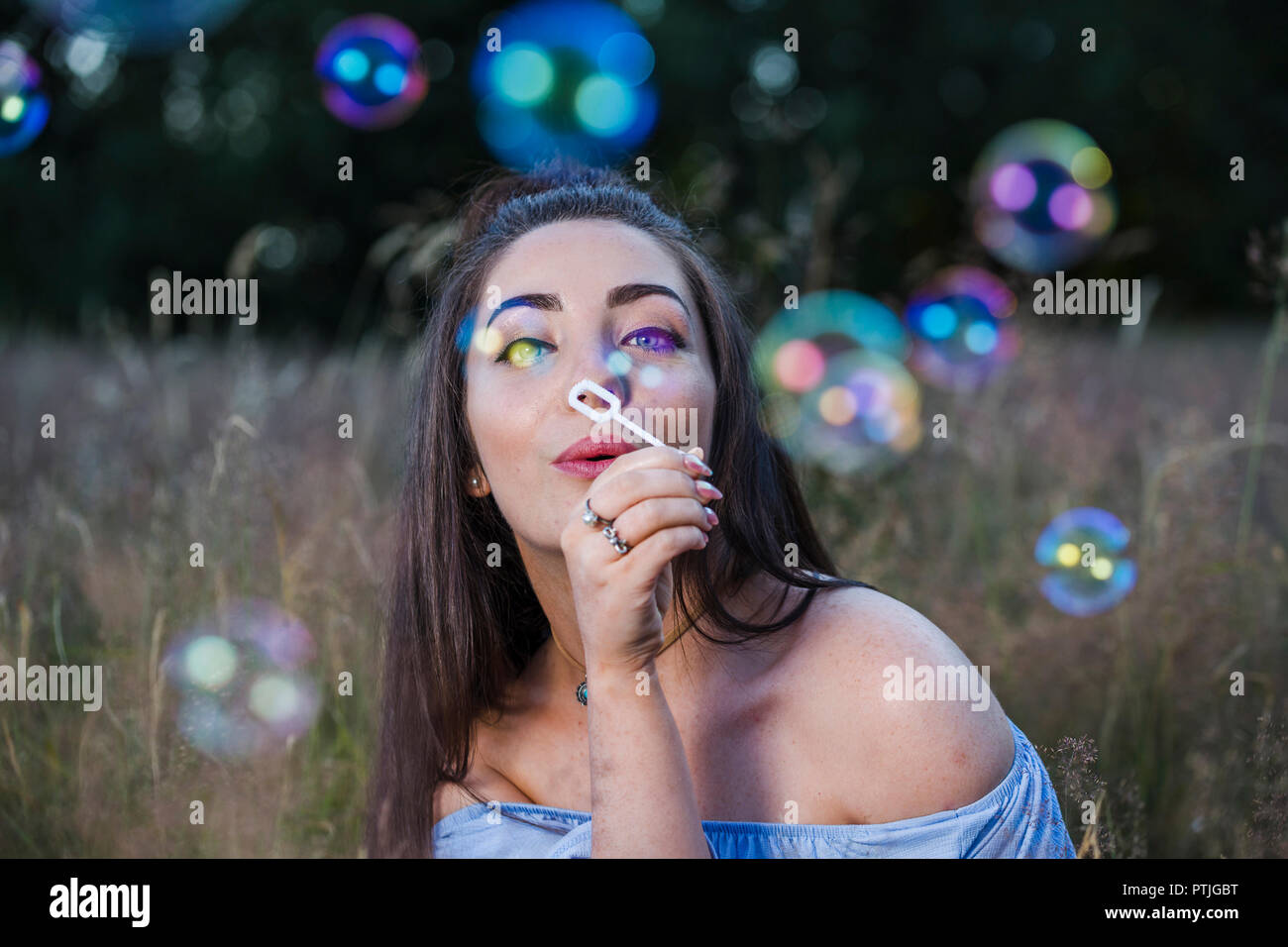 Une jeune femme souffle bulles vers la caméra dans un pré. Banque D'Images