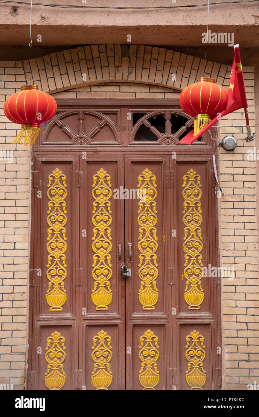 Lanterne chinoise et d'un drapeau plus cadenassé la porte en bois avec du verre brisé dans la vieille ville de nouveau voisinage Uigher à Kashgar, ou Kashi, Xinjiang, Chine. Banque D'Images
