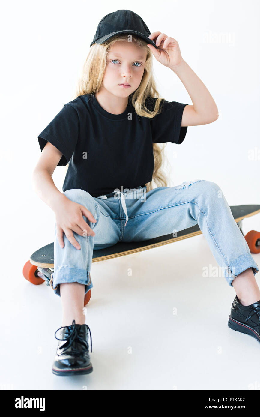 Portrait de kid en capuchon noir et t-shirt assis sur longboard et looking at camera isolated on white Banque D'Images