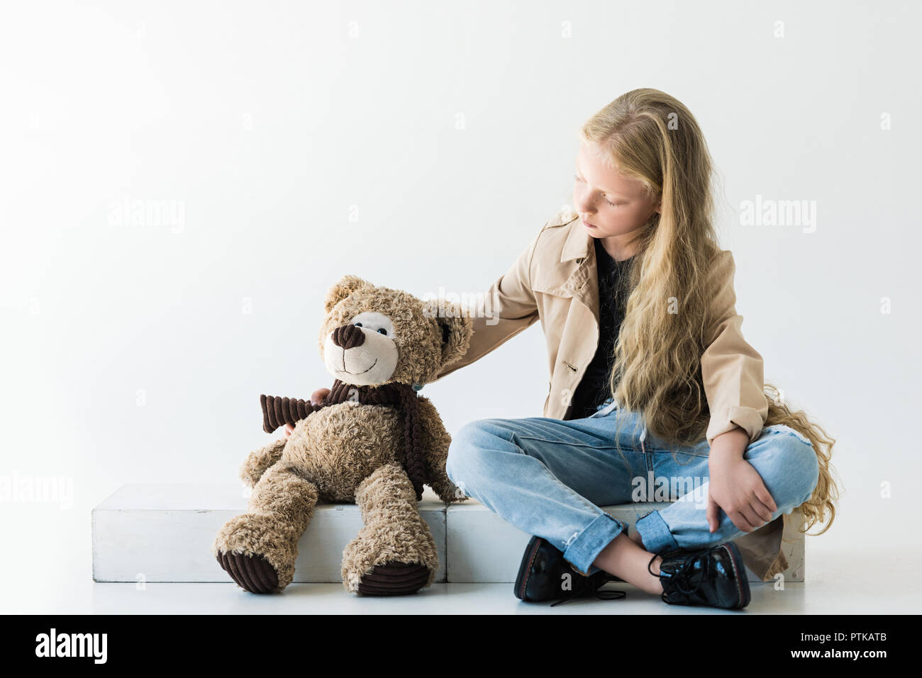 Sur toute la longueur de l'élégant mignon enfant assis et regardant teddy bear on white Banque D'Images