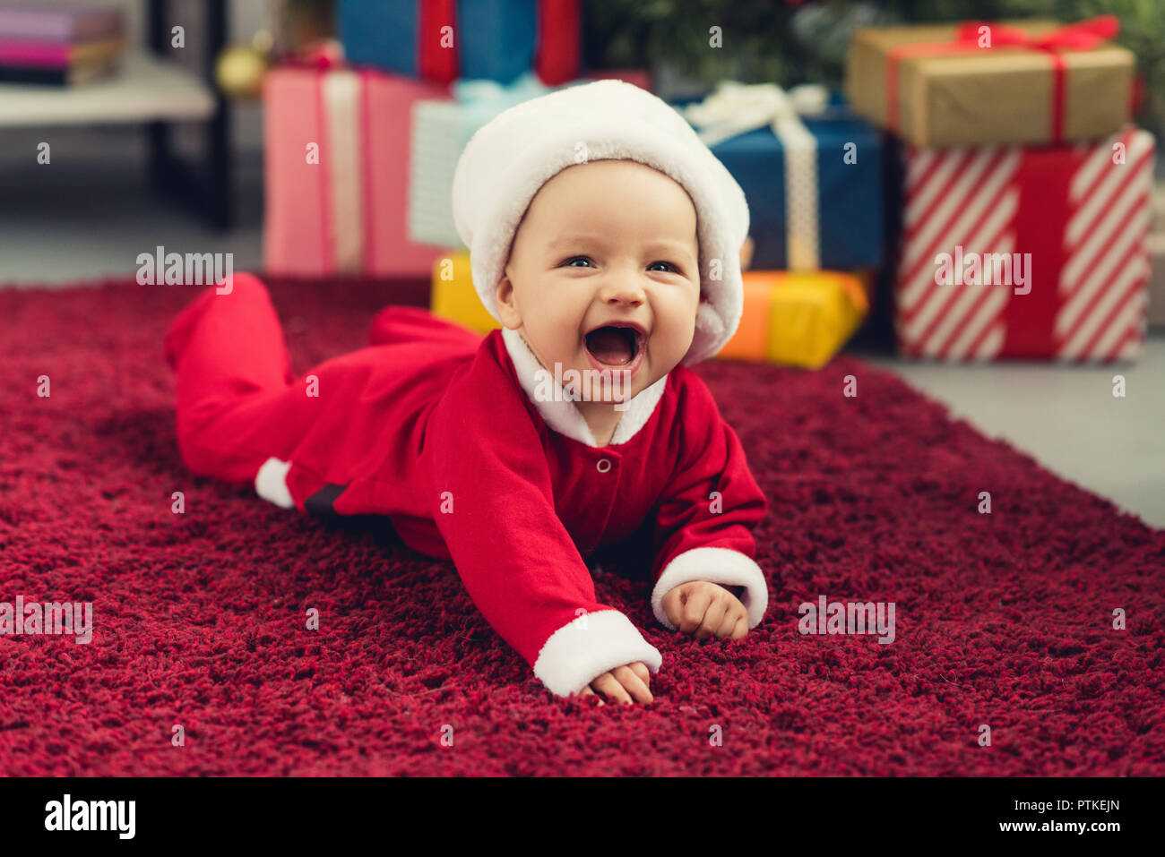 Rire Petit Bebe En Costume Pere Noel Allonge Sur Tapis Rouge En Face De L Arbre De Noel Et Cadeaux Photo Stock Alamy