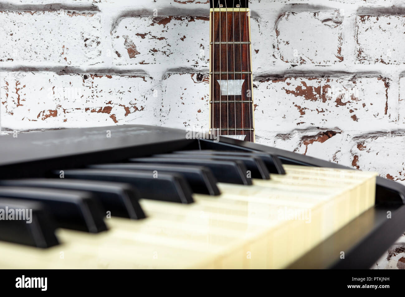 Guitare électrique appuyé contre un mur peint en blanc vieilli derrière un clavier de piano Banque D'Images