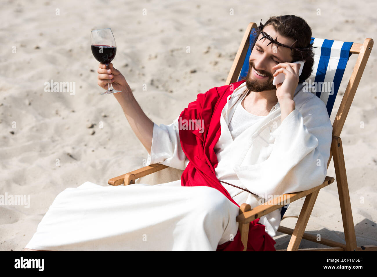 Smiling Jésus reposant sur une chaise longue avec verre de vin et de parler  par smartphone dans desert Photo Stock - Alamy