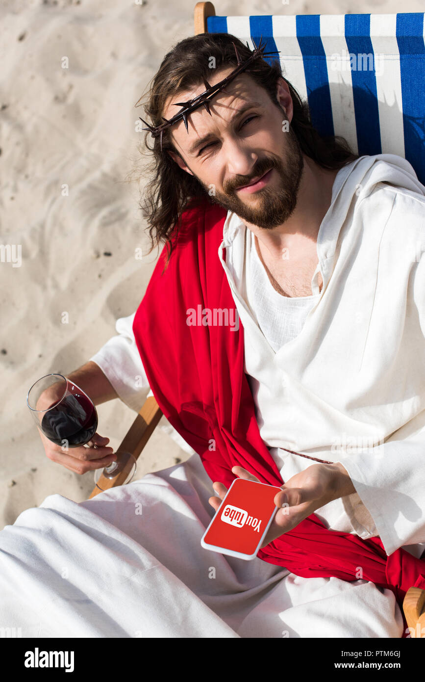 Jésus se reposant sur une chaise longue avec verre de vin et holding  smartphone avec youtube page in desert Photo Stock - Alamy