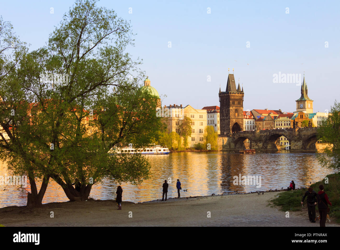 Prague, République tchèque : les touristes à pied au coucher du soleil par la rive de la Vltava, par le Pont Charles. Banque D'Images