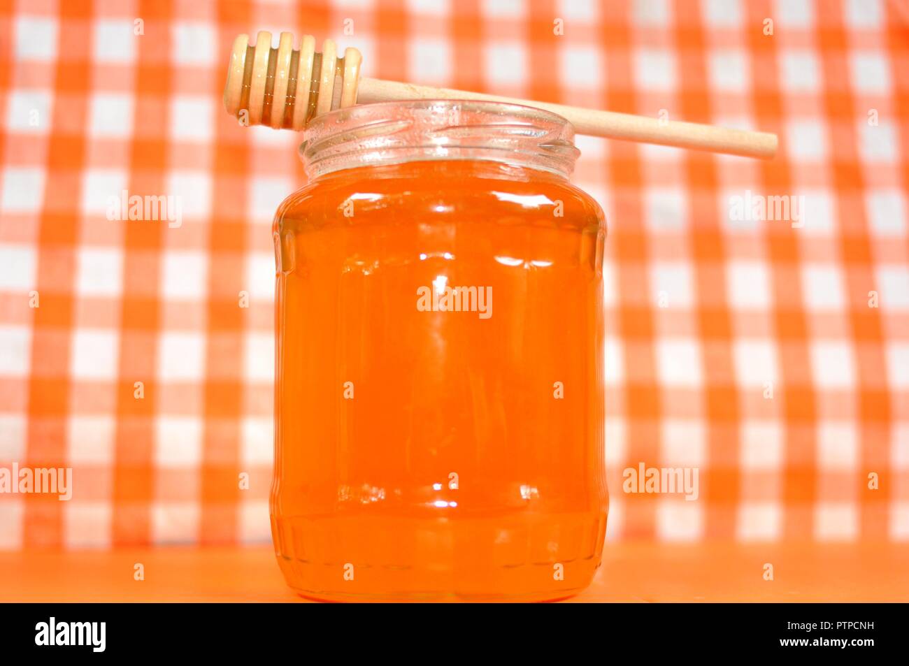 Pot de miel orange doré et bâton en bois debout de balancier sur la bouche du pot. Arrière-plan de la grille blanche et orange, gros plan, copiez l'espace. Banque D'Images
