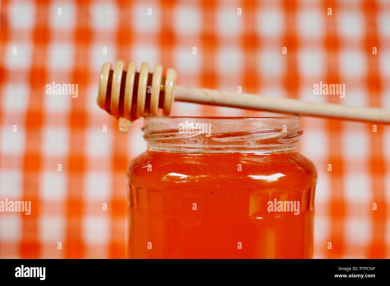 Pot de miel orange doré et bâton en bois debout de balancier sur la bouche du pot. Grille blanche et orange, gros plan, arrière-plan copie espace, sélective Banque D'Images