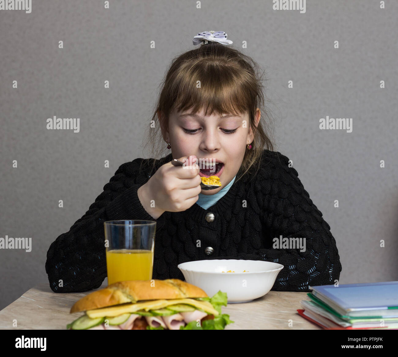 Une fille de 9 à 10 ans petit déjeuner avant de partir pour l'école, sur la table d'un manuel et d'un sandwich Banque D'Images