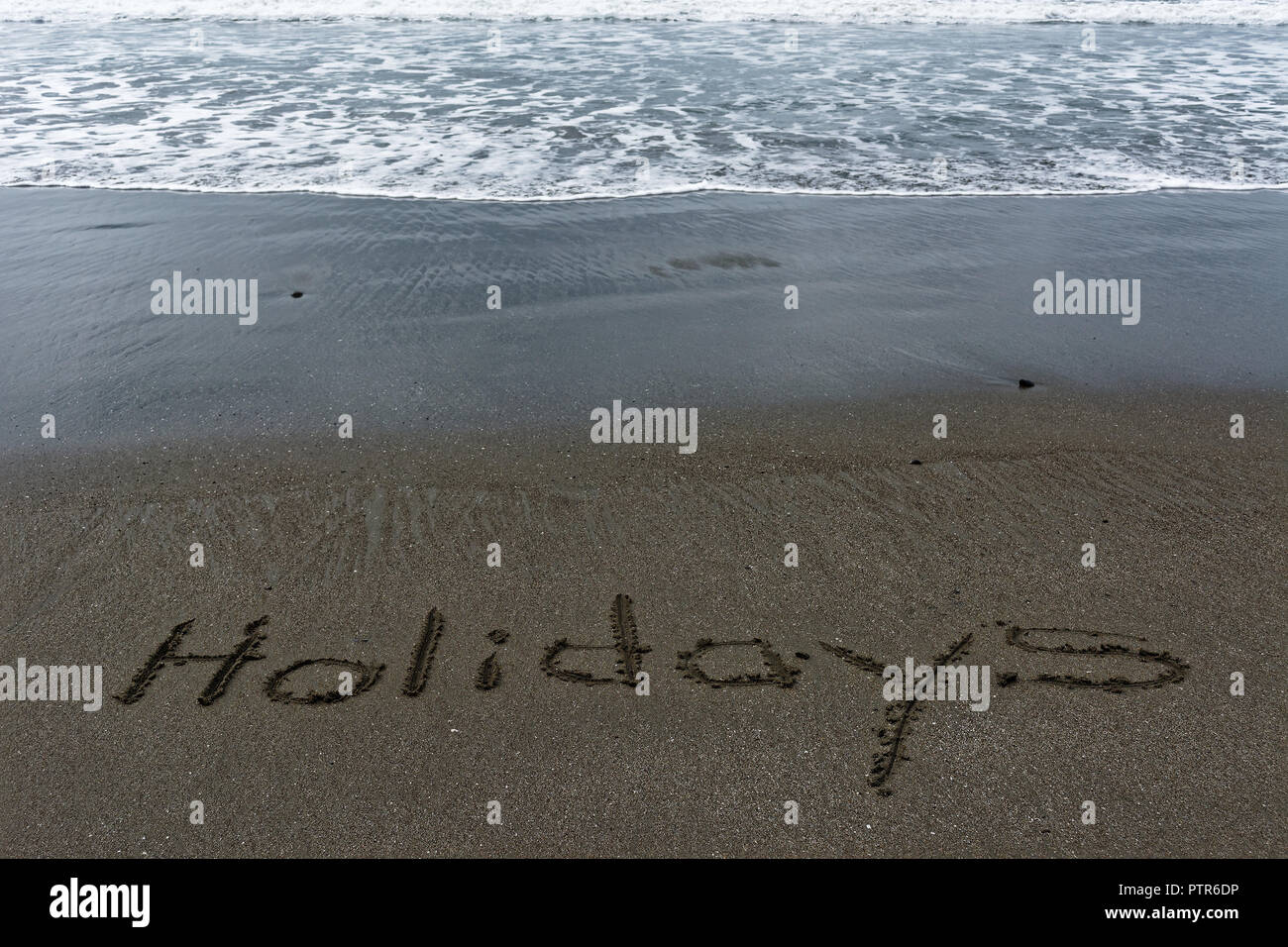 Clapotis des vagues vers le mot vacances écrit dans le sable. Banque D'Images