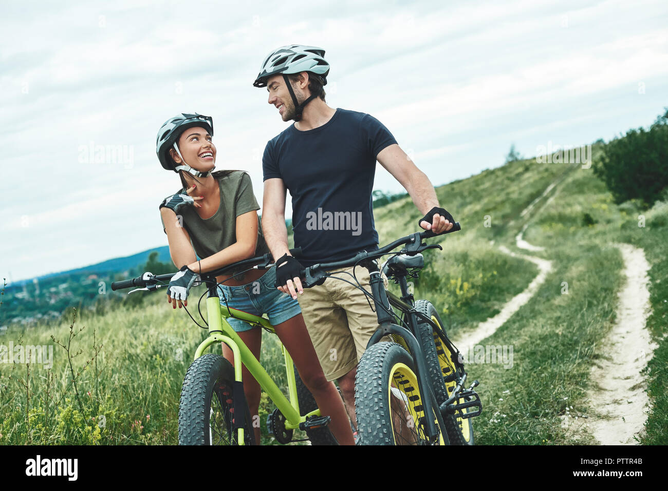 Jeune couple sont belles à parler de vertes collines. Ils portent des équipements protégés et équitation fatbikes Banque D'Images