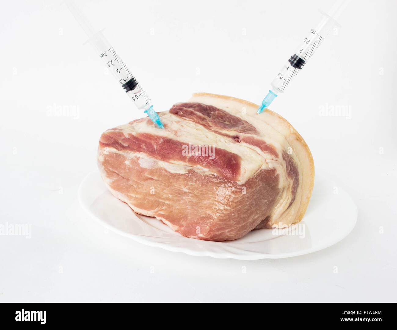Sur la plaque se trouve un morceau de viande de porc dans les seringues avec elle une hormone, fond blanc Banque D'Images