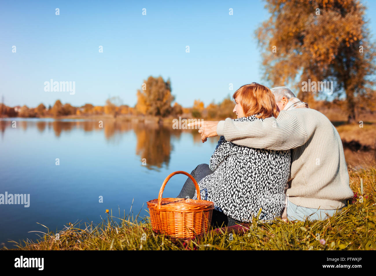 Senior couple having picnic par automne lac. Heureux l'homme et de la femme jouir de la nature et s'étreindre. Homme pointant en distance Banque D'Images