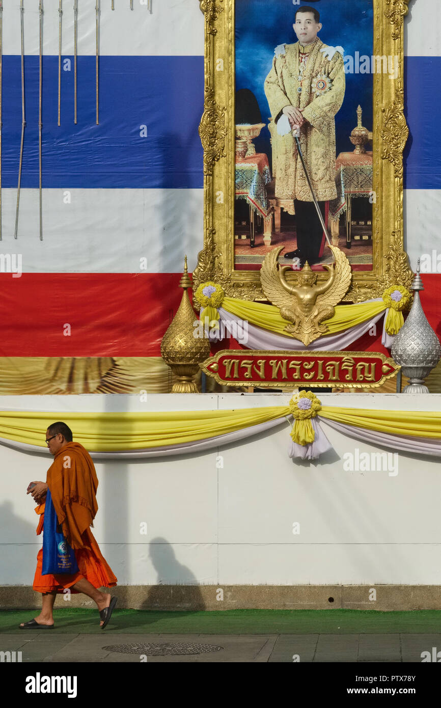 Un moine bouddhiste à Bangkok, Thaïlande, passe sous un portrait du roi Maha Vajiralongkorn et les couleurs nationales Thaï Banque D'Images