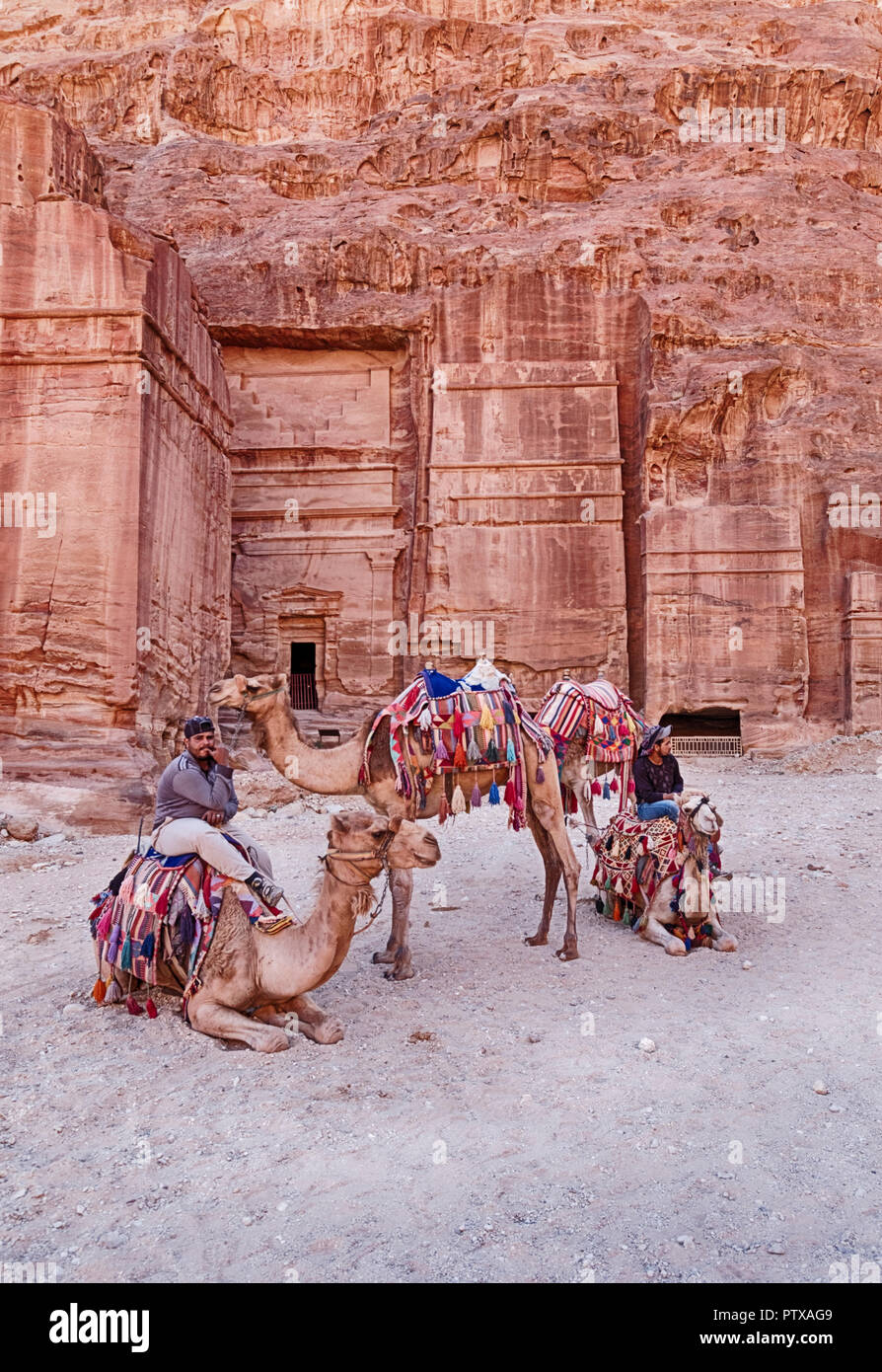PETRA, JORDANIE - 15 juin 2018 : Quatre chameaux et leurs chauffeurs attendent pour des tours en face d'une des anciennes tombes de Petra qui sont taillées dans le roc Banque D'Images