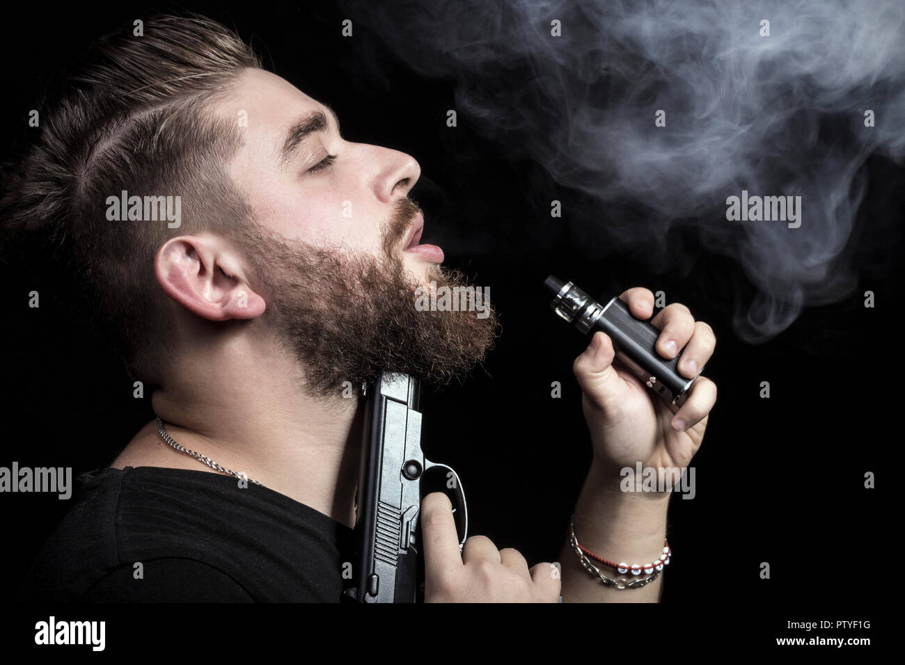 Un homme avec une arme à feu à son menton fume une cigarette électronique, le concept de l'instant ou mort lente, image de fond Banque D'Images