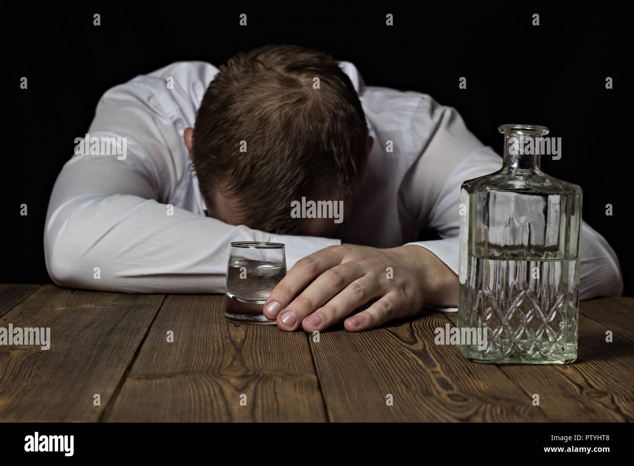 Un homme ivre se trouve sur une table, dans sa main un verre de vin avec de l'alcool, un fond noir Banque D'Images