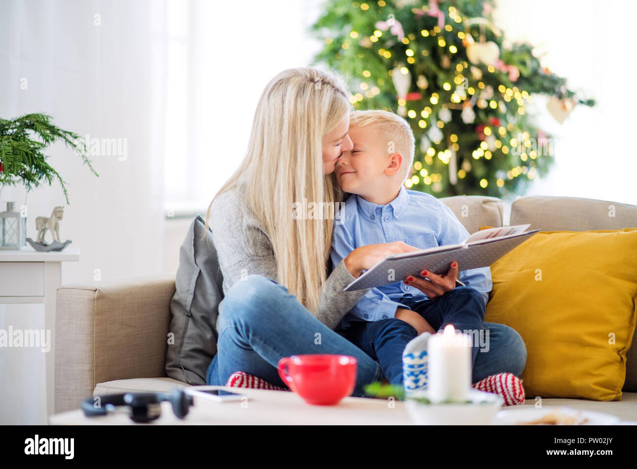 Une mère et petit garçon assis sur un canapé à la maison au moment de Noël, la lecture d'un livre. Banque D'Images