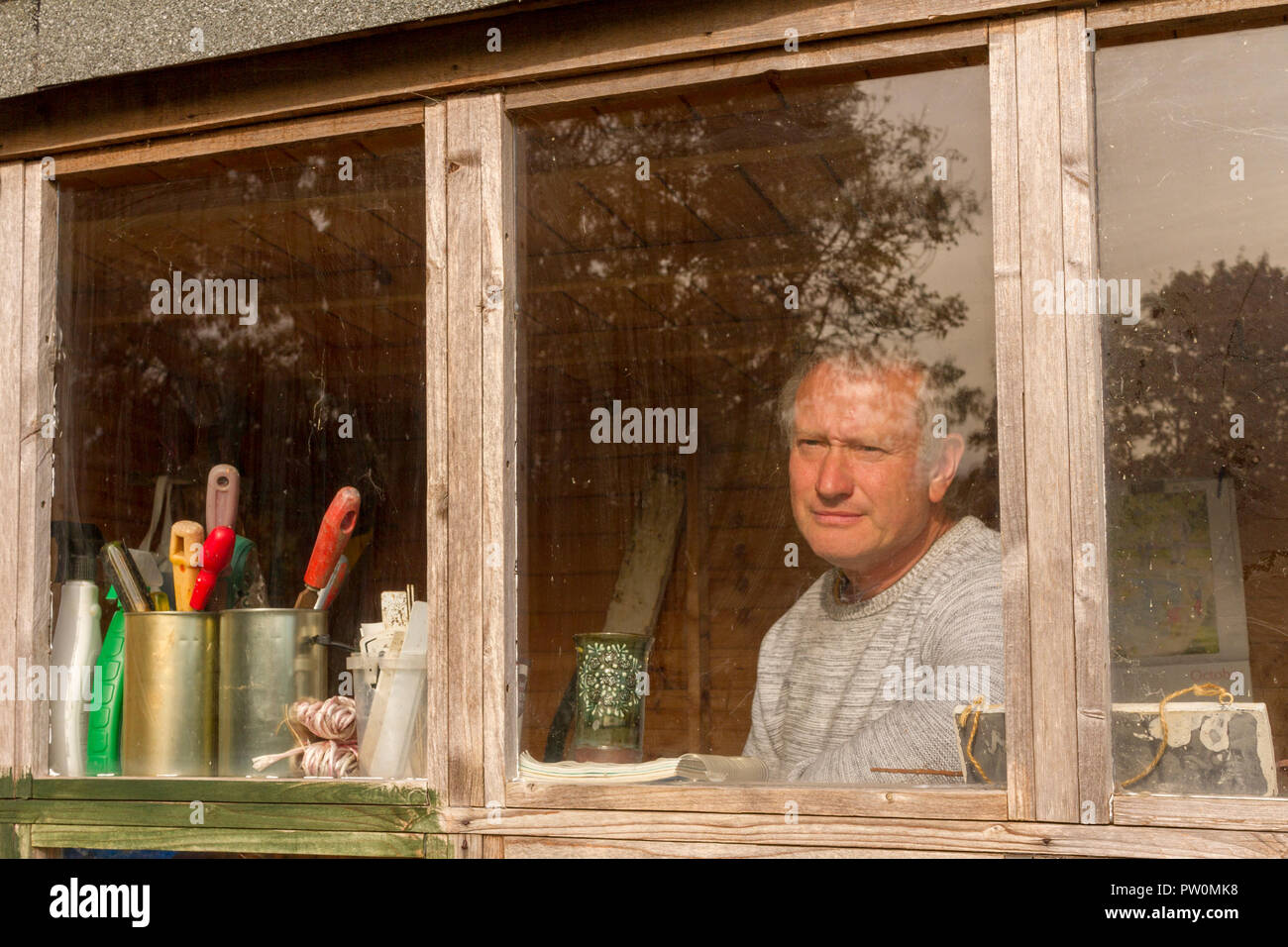 Un homme d'âge moyen blanc à la recherche d'abri de jardin fenêtre, contemplant son attribution et de réfléchir à ses projets pour l'avenir Banque D'Images
