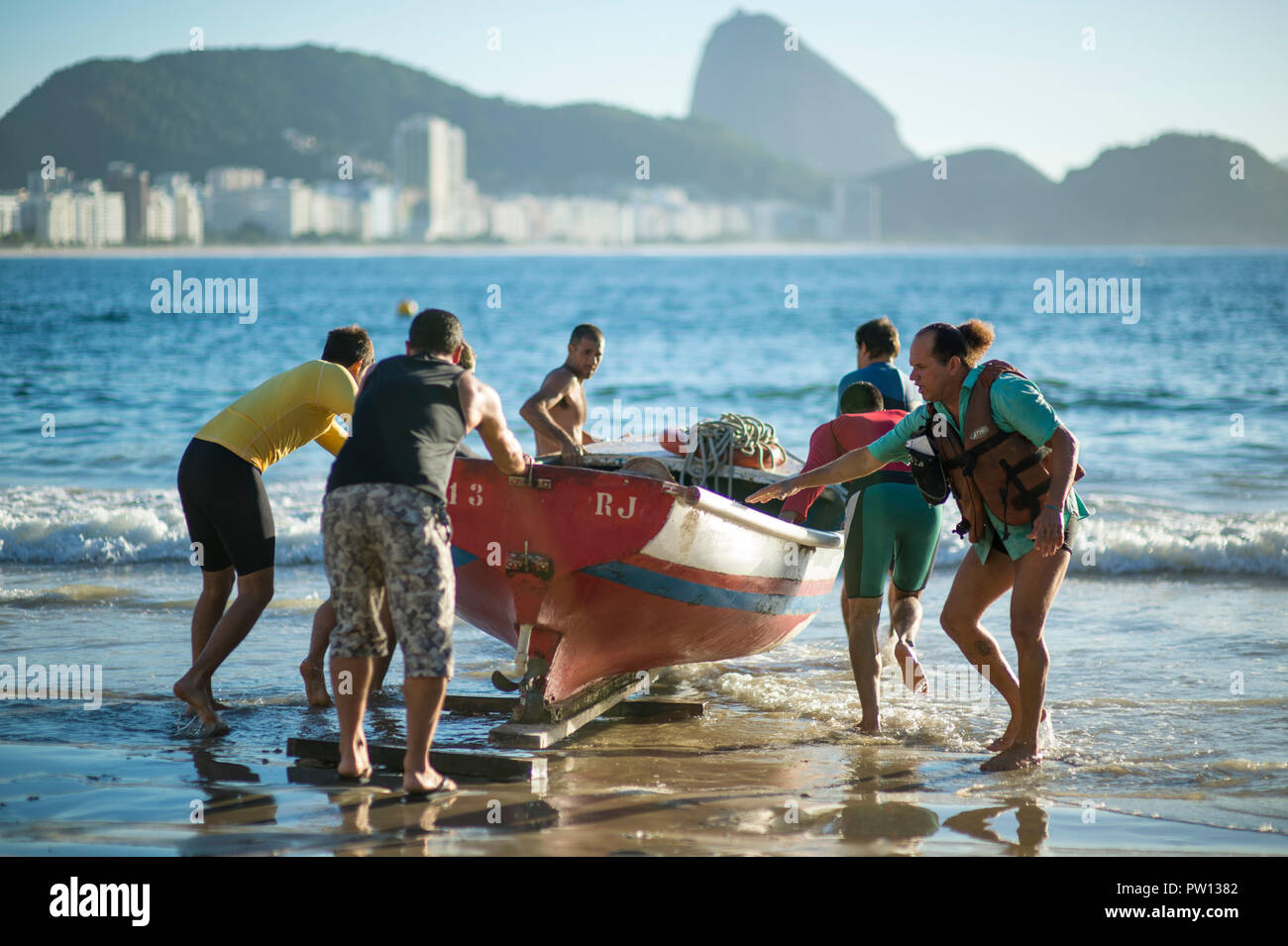 RIO DE JANEIRO - circa 2018, Février : un groupe d'hommes brésilien aider à pousser un bateau de pêche dans l'océan à la plage de Copacabana. Banque D'Images