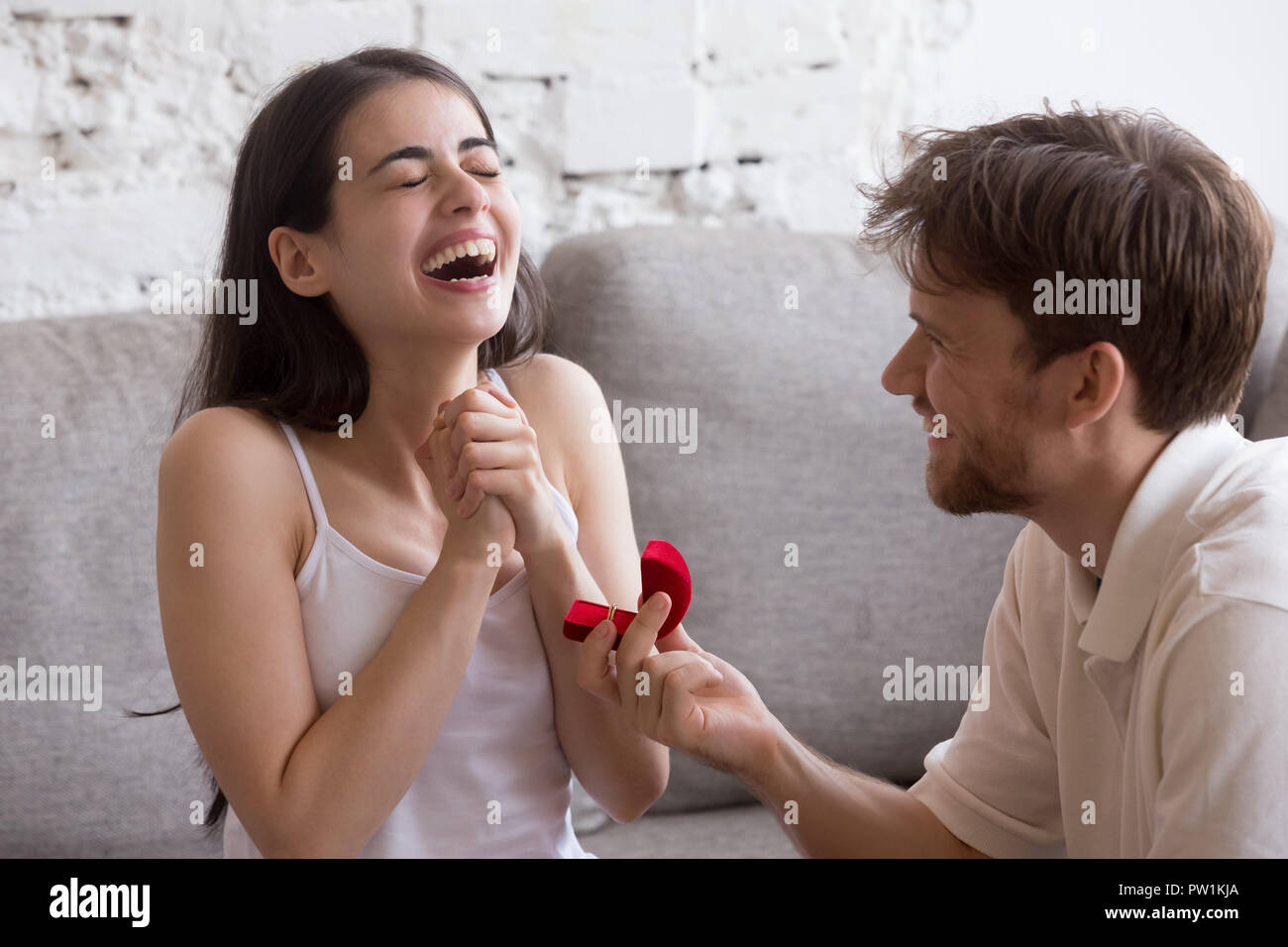 Heureux jeune homme propose à sa copine assise sur canapé Banque D'Images
