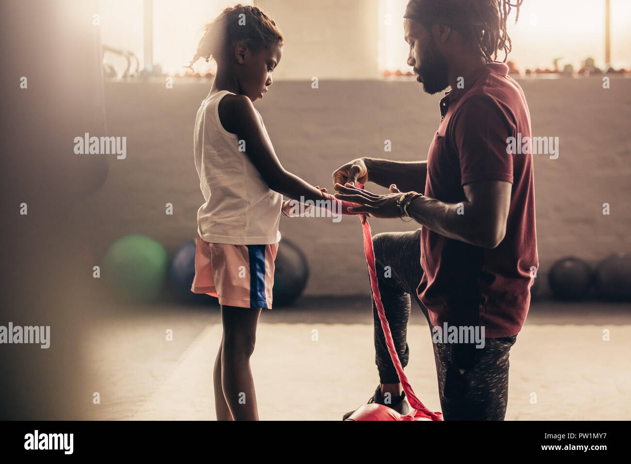 Kid boxe mettre la main recouverte d'un bandage avant de mettre des gants de boxe. Vue latérale d'un gamin avec son entraîneur de boxe à un club de boxe avec Sun Banque D'Images