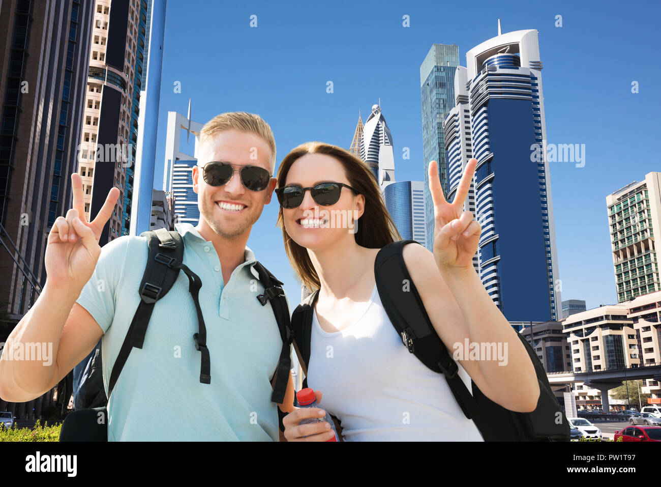 Portrait Of Happy Young Couple Gesturing Peace Sign In City Banque D'Images