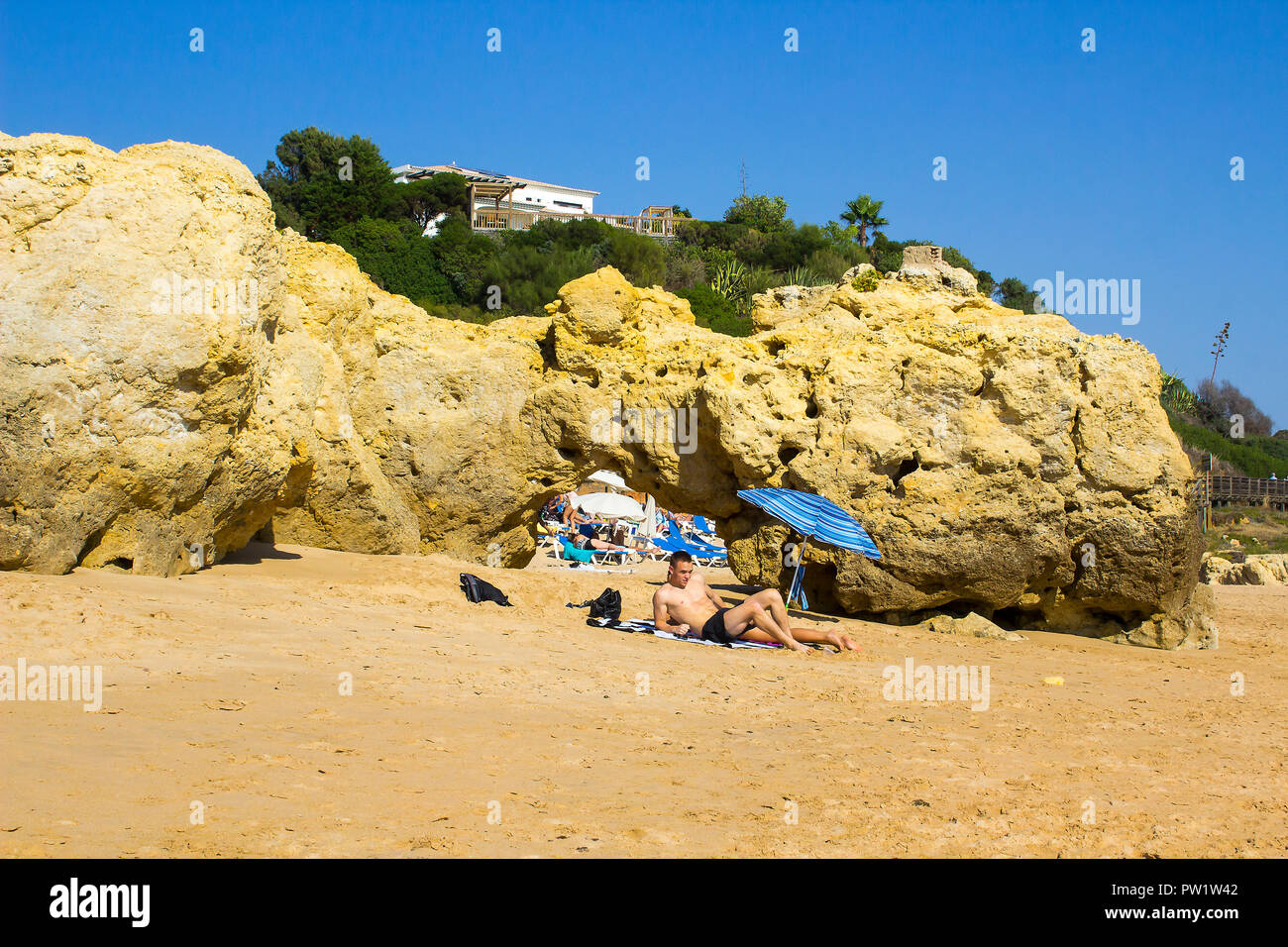 29 septembre 2018 Un couple s'asseoir au soleil à côté d'un petit soleil brolly sur une partie éloignée de la plage Oura Praia dans Albferiah sur l'Algarve au Portugal Banque D'Images