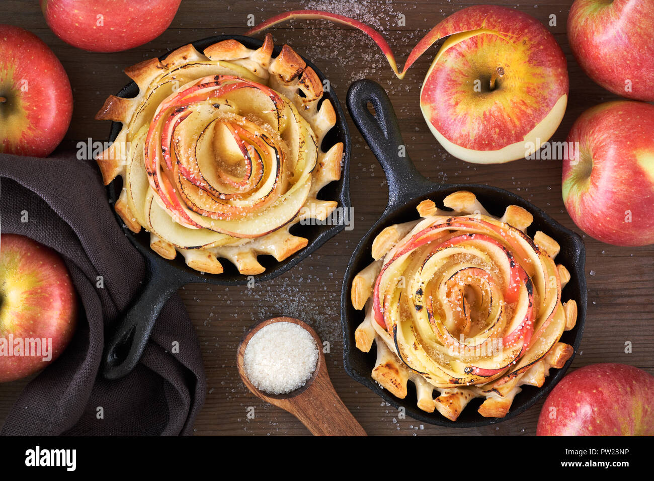 Des feuilletés en forme de rose avec des tranches de pomme au four dans une  poêle de fer. Haut lay sur planche de bois avec des pommes et du sucre  Photo Stock -
