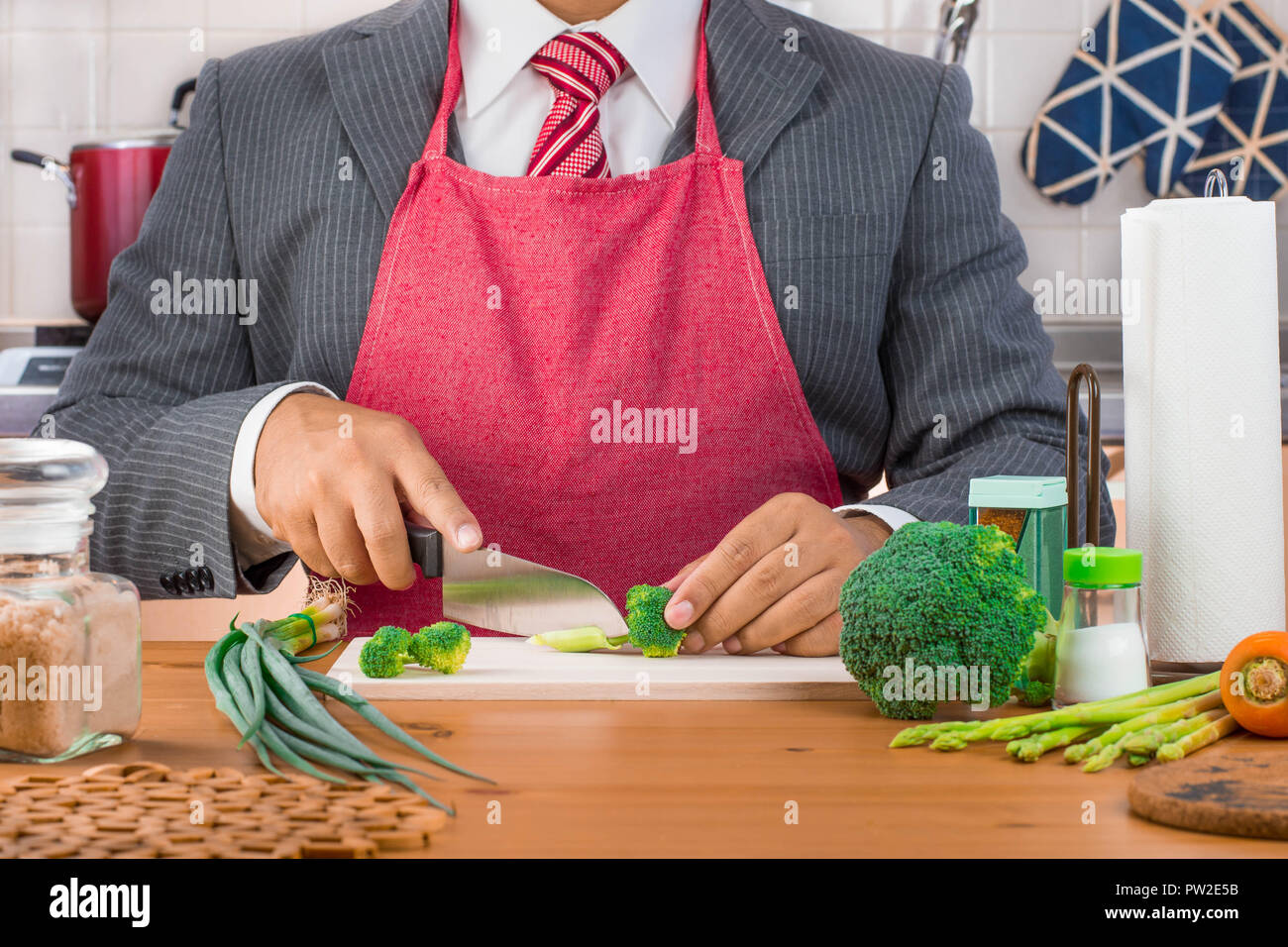 Un homme d'affaires, père, mari en costume et cravate rouge portant un  tablier rouge et couper le brocoli et les légumes avec un couteau sur une  planche à découper en bois Photo