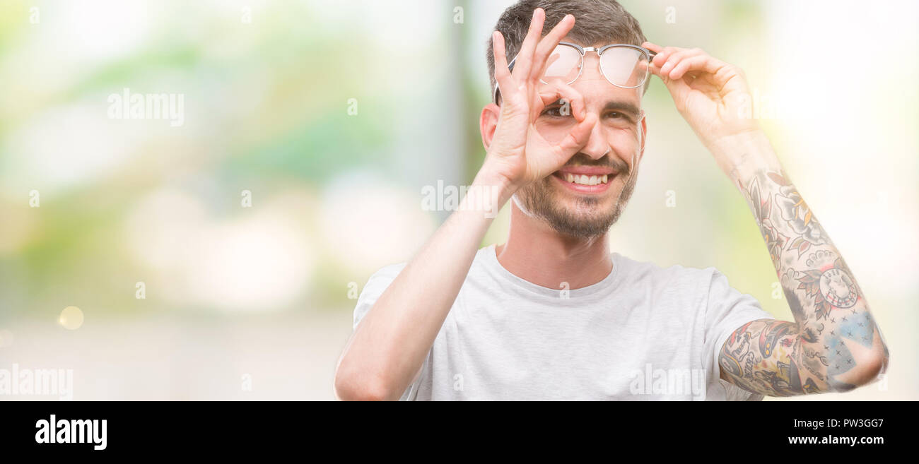 Les jeunes adultes faisant l'homme tatoué ok geste avec la main en souriant, les yeux regardant à travers les doigts avec un visage heureux. Banque D'Images
