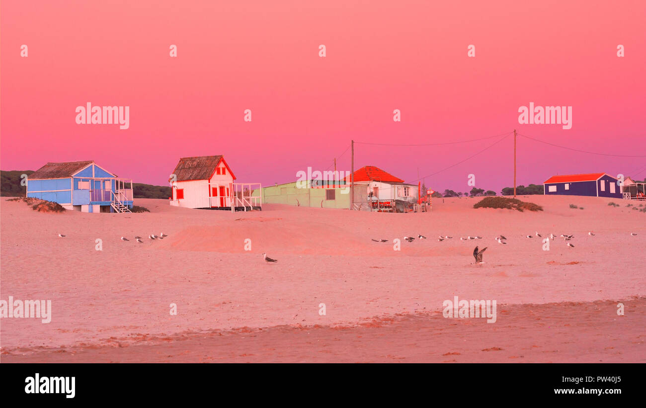 Maisons de Plage colorés sur la plage de Costa da Caparica à Lisbonne, au coucher du soleil avec un ciel orange et vue sur la plage de sable doré Banque D'Images