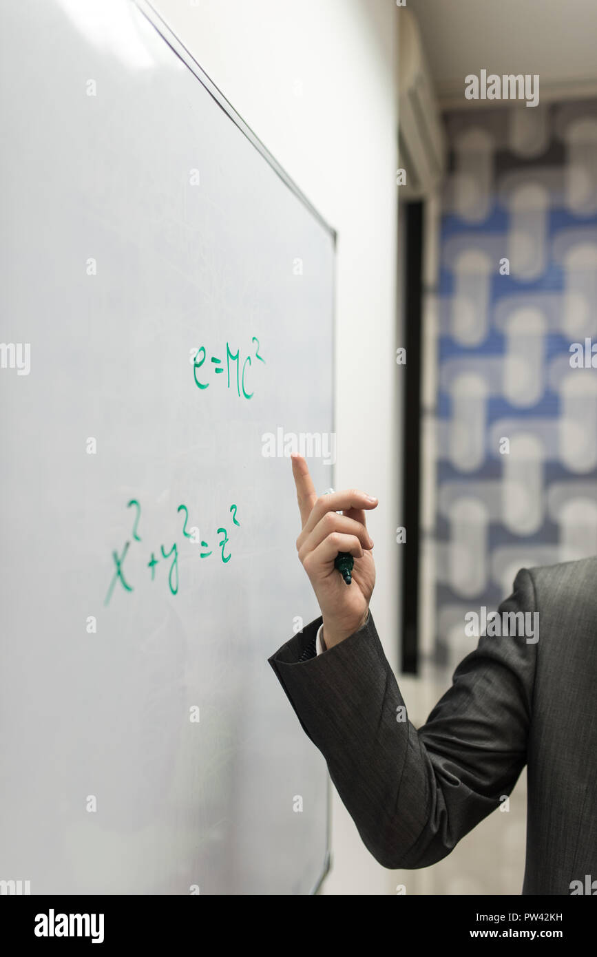 Libre du professeur pointant vers une formule d'équivalence masse-énergie écrit sur un tableau blanc. Banque D'Images