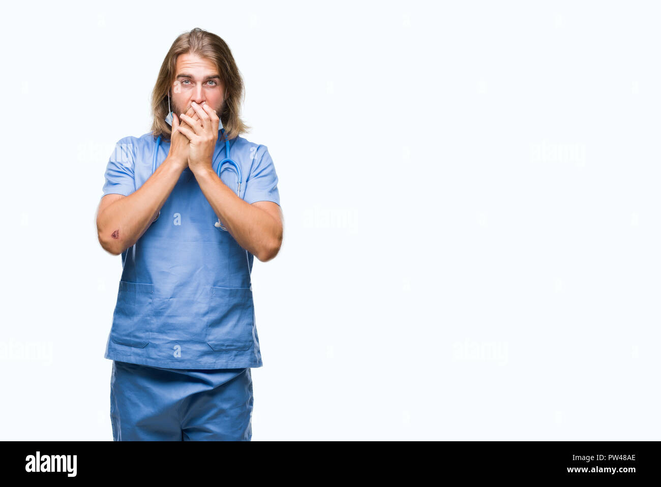 Beau jeune homme médecin aux cheveux longs sur fond isolé choqué couvrant la bouche avec les mains pour l'erreur. Concept Secret. Banque D'Images