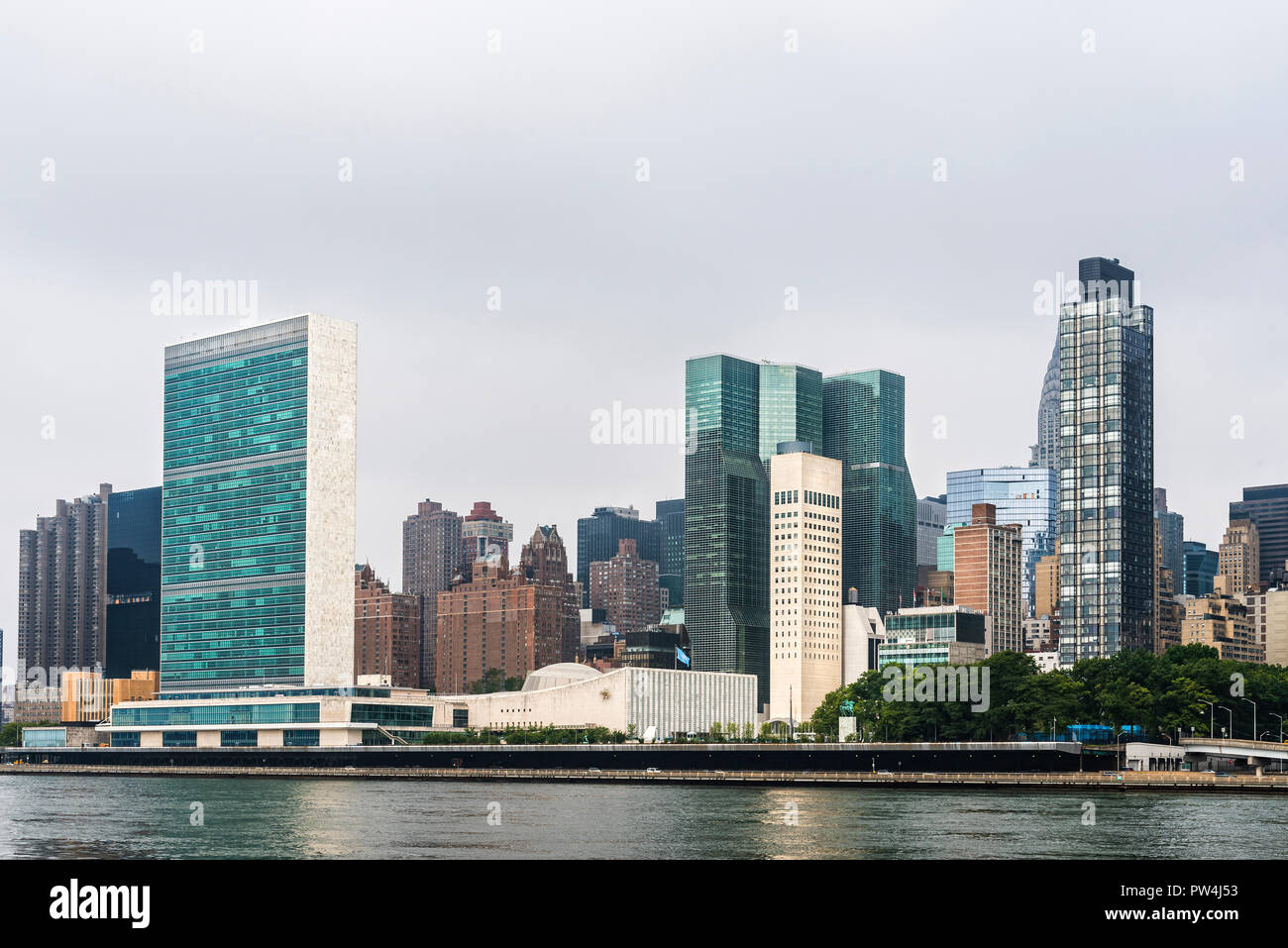 Les bâtiments modernes par East River contre ciel nuageux en ville Banque D'Images
