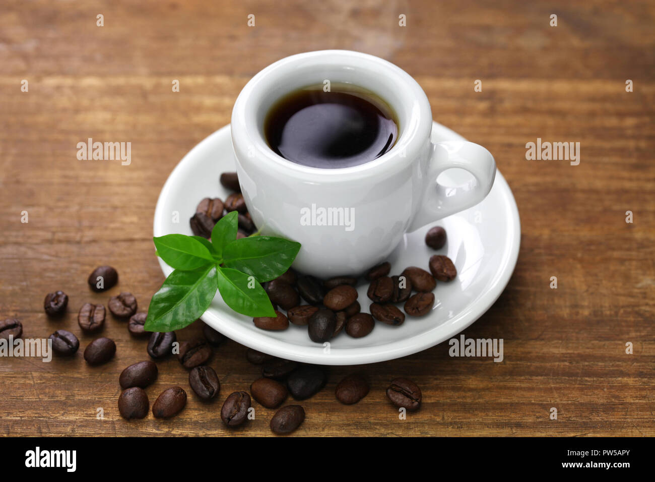 Une tasse de café noir avec des grains de café torréfié et de feuilles sur fond blanc Banque D'Images