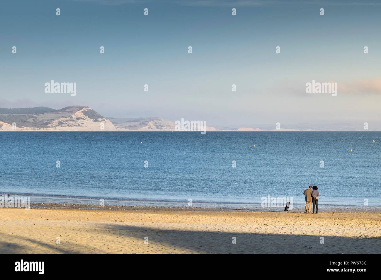 Un couple et leur chien sur la plage de Lyme profitant de la lumière du soir à la ville côtière de Lyme Regis dans le Dorset. Banque D'Images Un couple et leur chien sur la plage de Lyme profitant de la lumière du soir à la ville côtière de Lyme Regis dans le Dorset. Banque D'Images