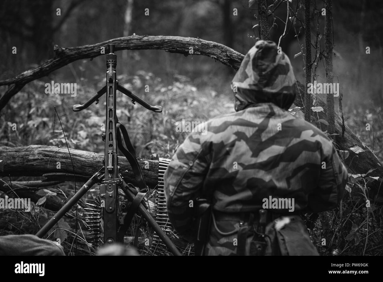 Non cachés de la reconstitution médiévale habillé en soldat de la Wehrmacht allemande assis avec une mitrailleuse dans une embuscade dans la forêt. Photo en noir et blanc. Banque D'Images