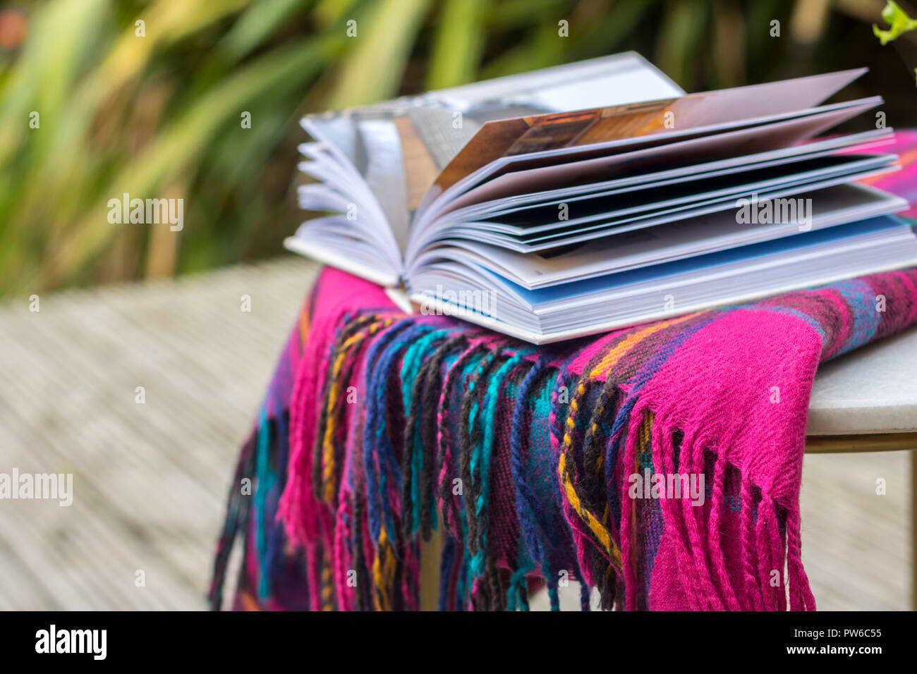 Couverture tartan livre ouvert sur une table de jardin à l'extérieur des maquettes, flatlay concept timeout, hygge, style de vie facile, meilleure vie brouillée détendue relaxant Banque D'Images