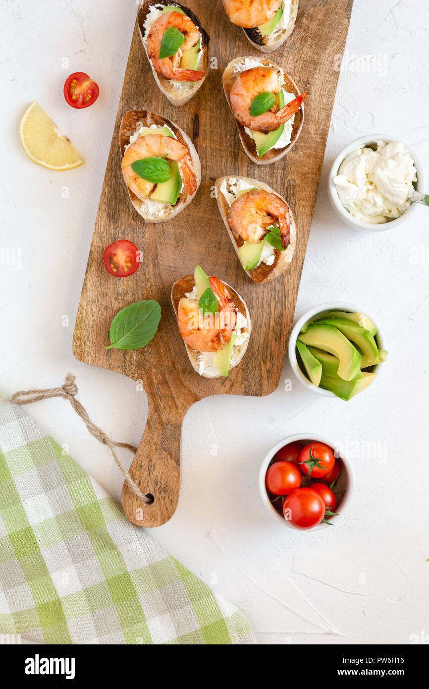 Snack-sandwiches italiens Bruschetta aux crevettes, avocat et fromage décoré par le basilic. Banque D'Images