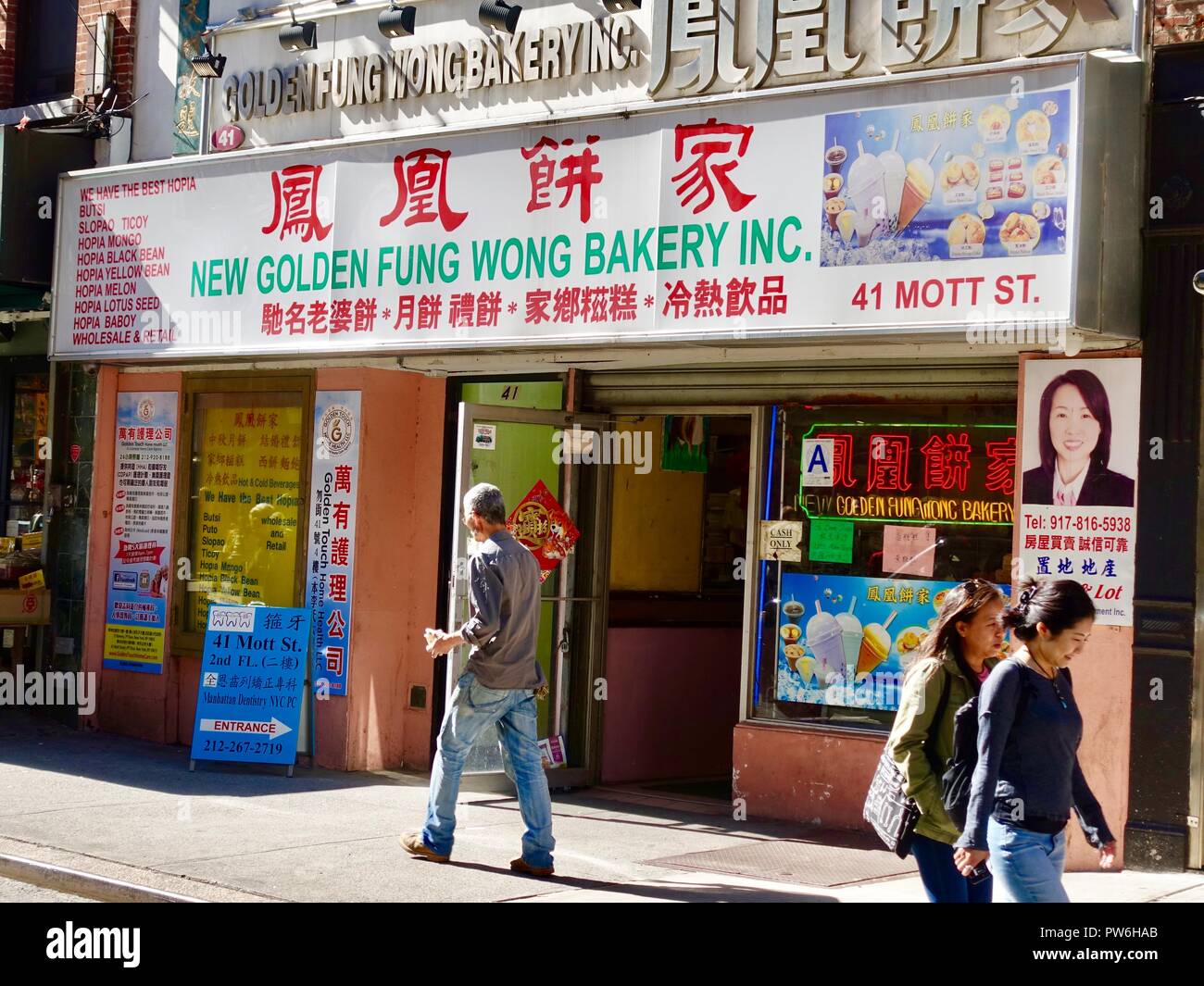 Des Asiatiques passant devant la New Golden Fung Wong Bakery, Inc, Mott Street, New York, NY, ÉTATS-UNIS. Banque D'Images