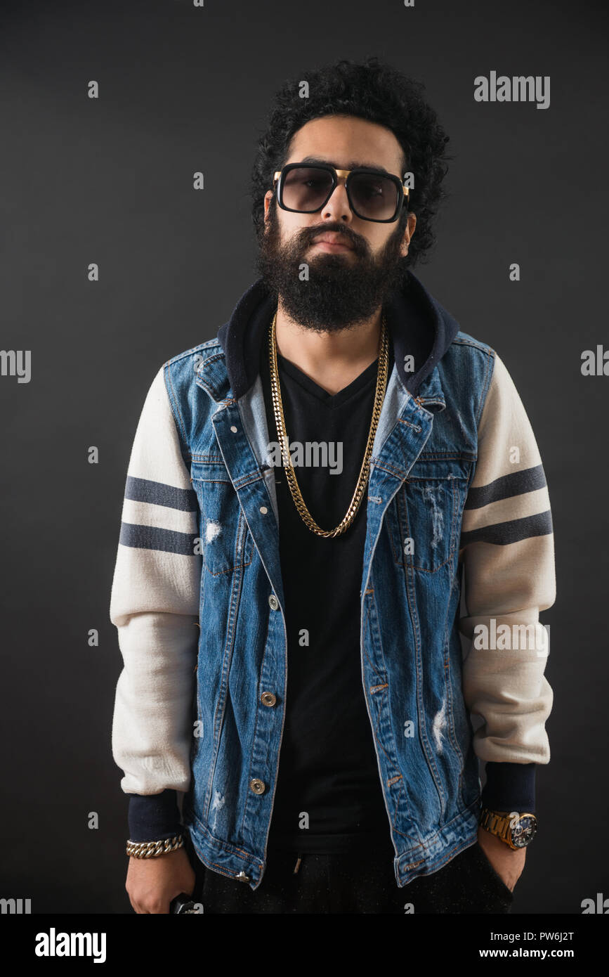 Jeune homme barbu réfléchie avec chaîne en or et jeans pull et lunettes de  soleil. Homme tenant un mod Photo Stock - Alamy