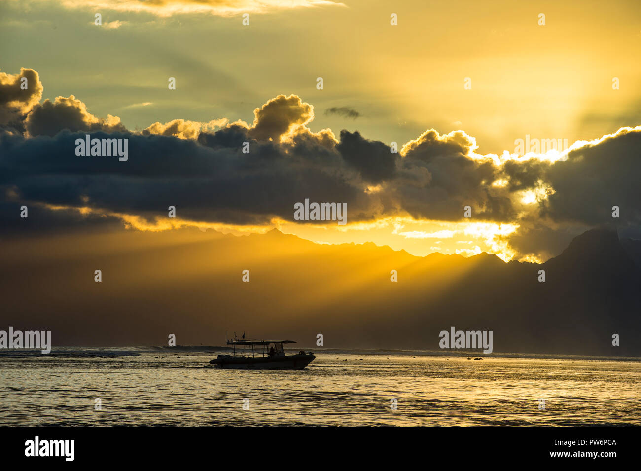 Silhouette d'un petit bateau au coucher du soleil, les rayons du soleil à travers les nuages breakig sur Moorea, Papeete, Tahiti Banque D'Images