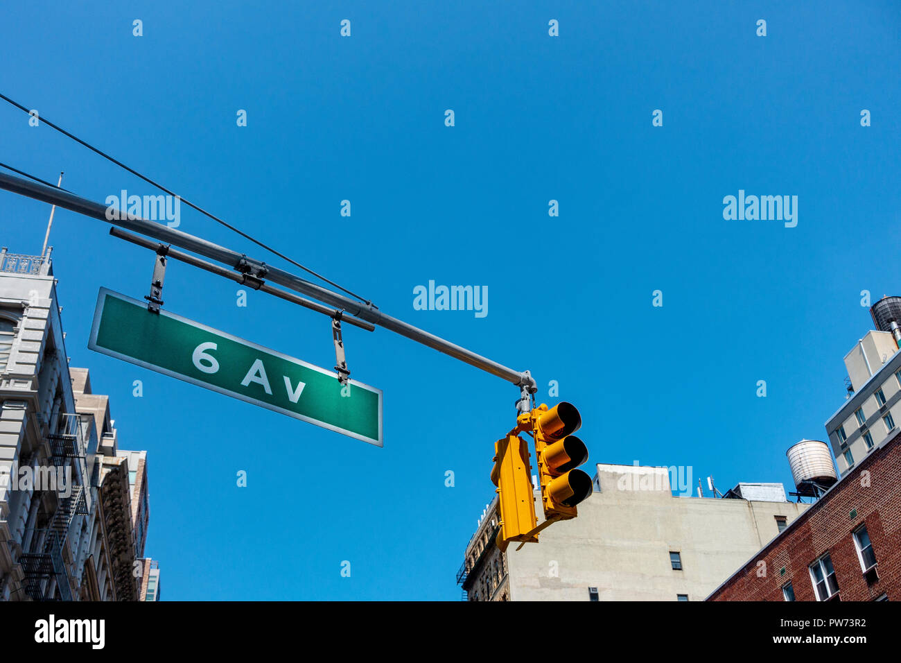 Signal jaune lumière suspendue au-dessus de New York City principale intersection de la 6e avenue, avec blanc vert street sign Banque D'Images