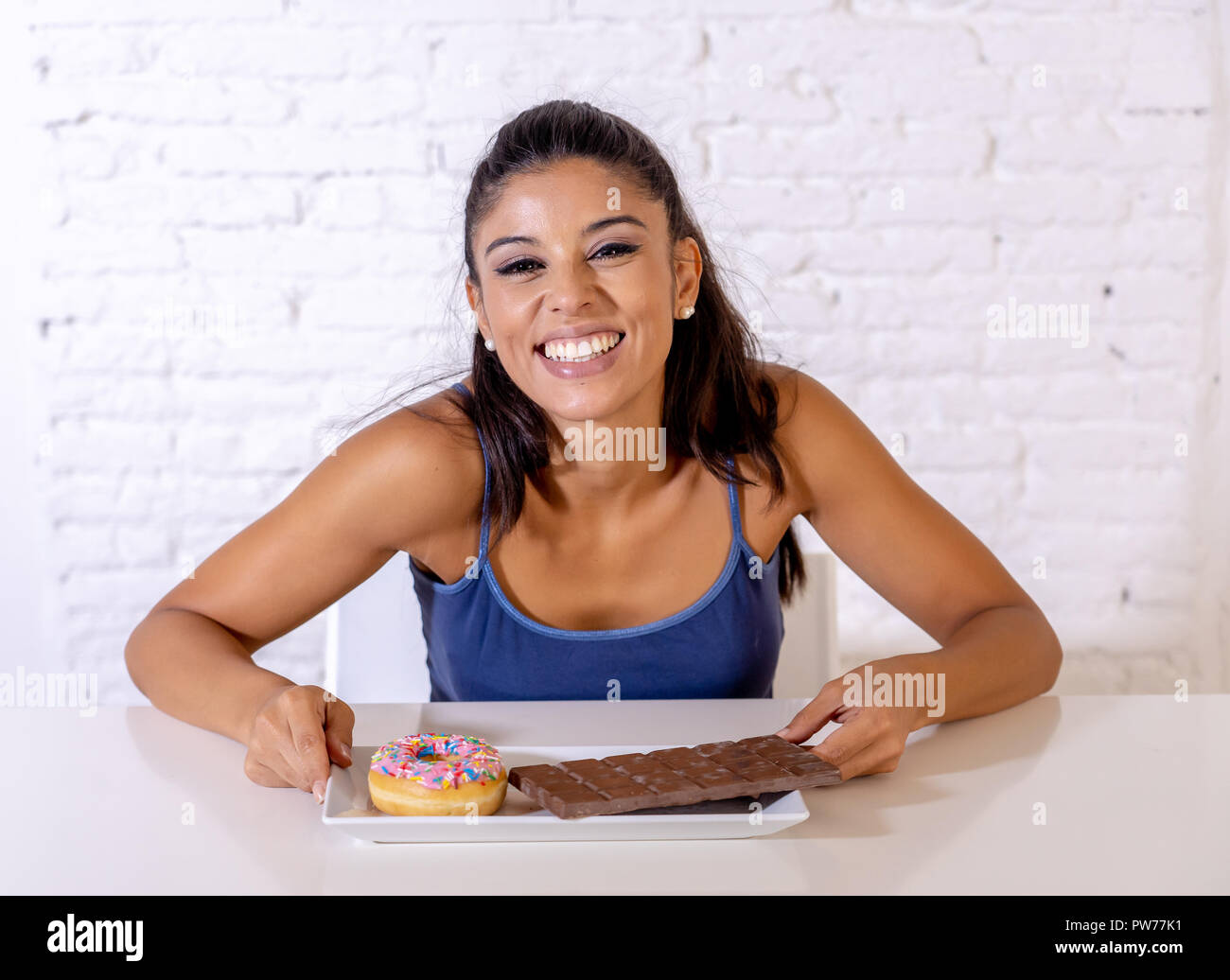 Young attractive woman sitting at table latine sur le point de manger du chocolat et des beignets à la excité et heureux en plus de l'alimentation, le sucre et l'unhealt chunky Banque D'Images